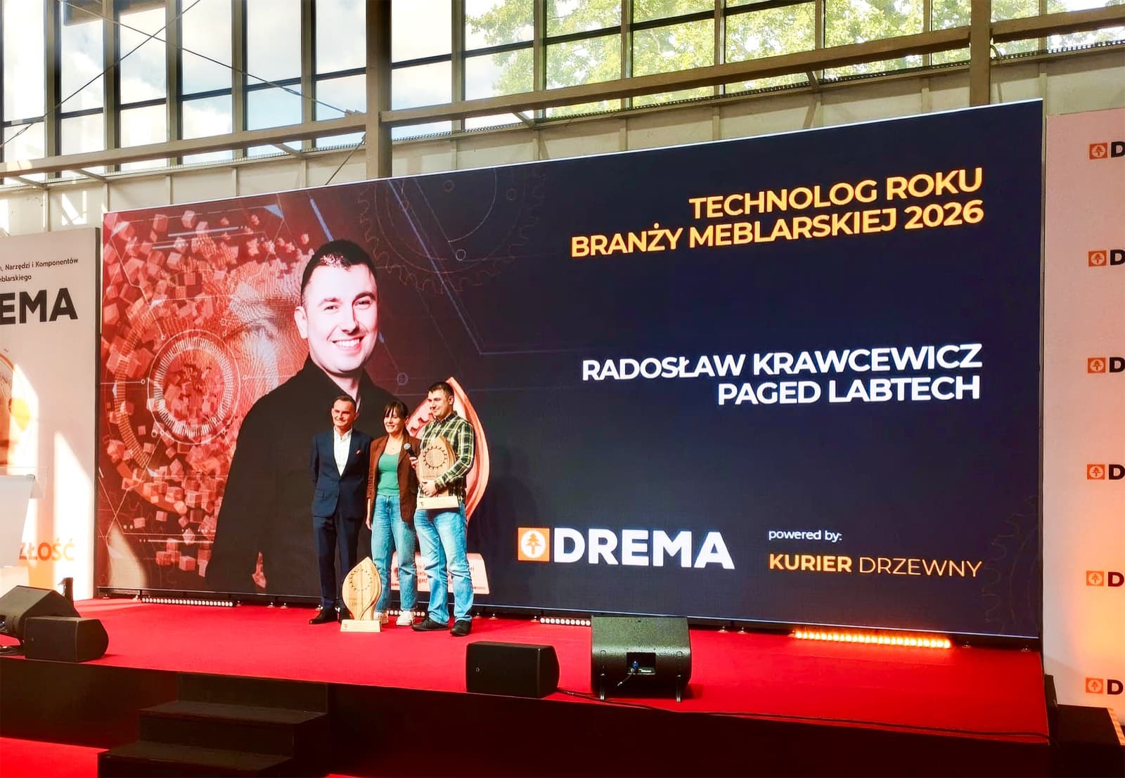 Radosław Krawcewicz mit der Auszeichnung auf der Bühne des III. Technologenforums der DREMA 2026, auf dem Bildschirm der Titel „Technologe des Jahres der Möbelbranche 2026“