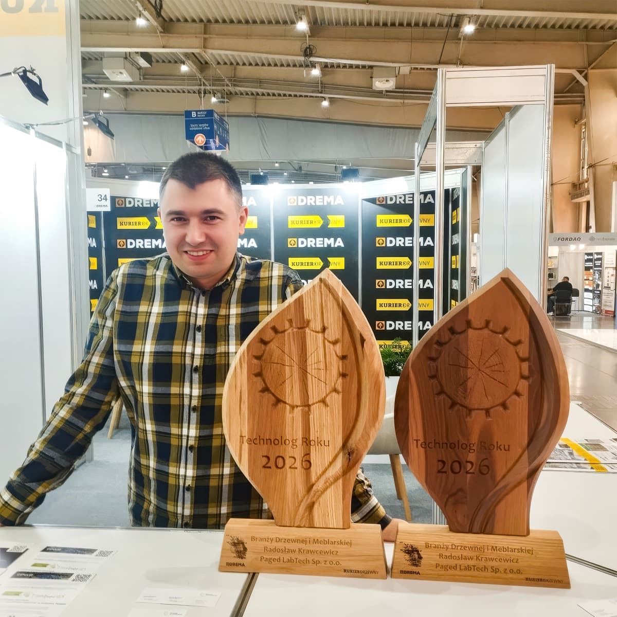 Radosław Krawcewicz an einem Messestand der DREMA hinter zwei hölzernen Trophäen mit der Aufschrift „Technolog Roku 2026“
